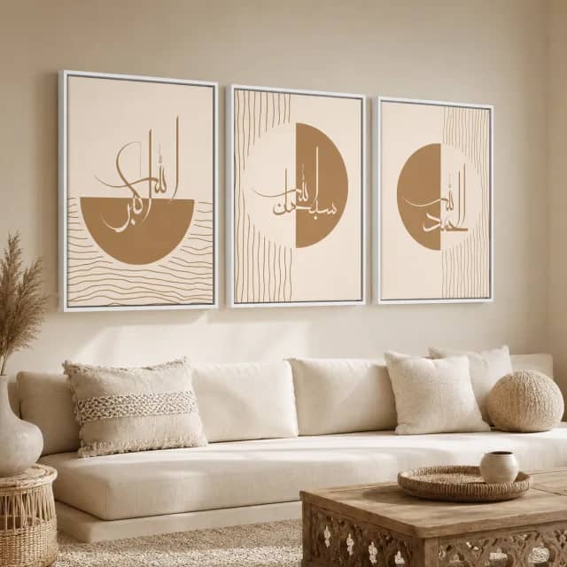 ثلاث لوحات إسلامية بإطارات بيضاء وخط ذهبي فوق أريكة بألوان حيادية.