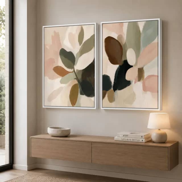 Two abstract botanical pieces in white frames above a softly styled bed